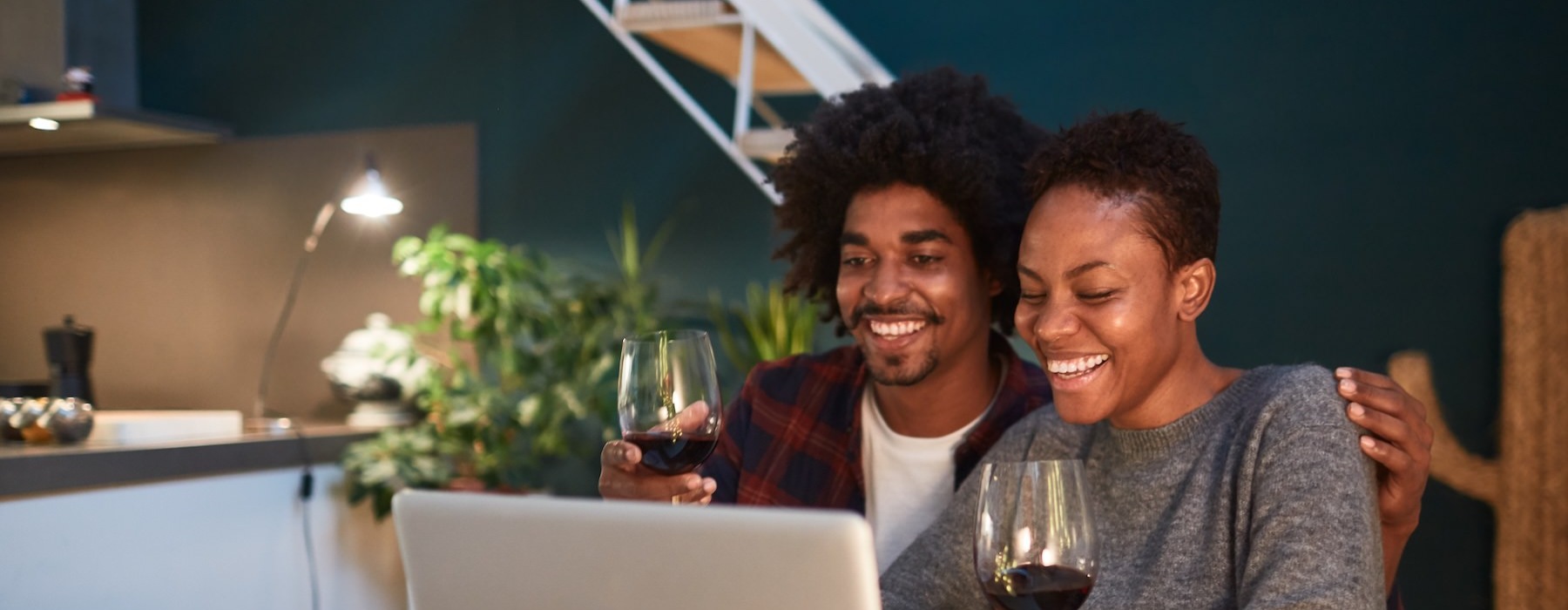 a couple of people sit at a table with a laptop and a glass of wine