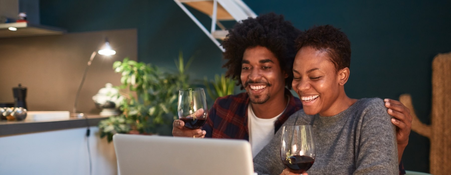 a couple of people sit at a table with a laptop and a glass of wine